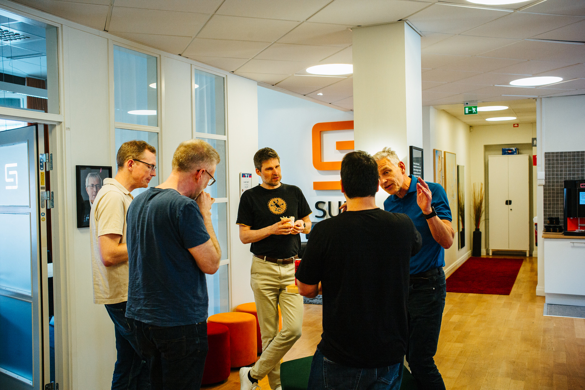 Fem personer står i korridoren på ett kontor och pratar med varandra